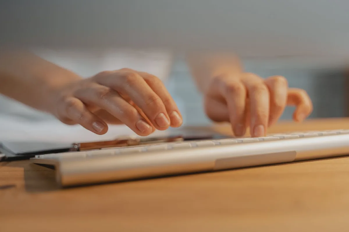 Análise Ergonômica do Trabalho Curitiba: o que sua empresa precisa cumprir Mãos digitando em um teclado branco, demonstrando tecnologia e produtividade. — Medicina Ocupacional Curitiba