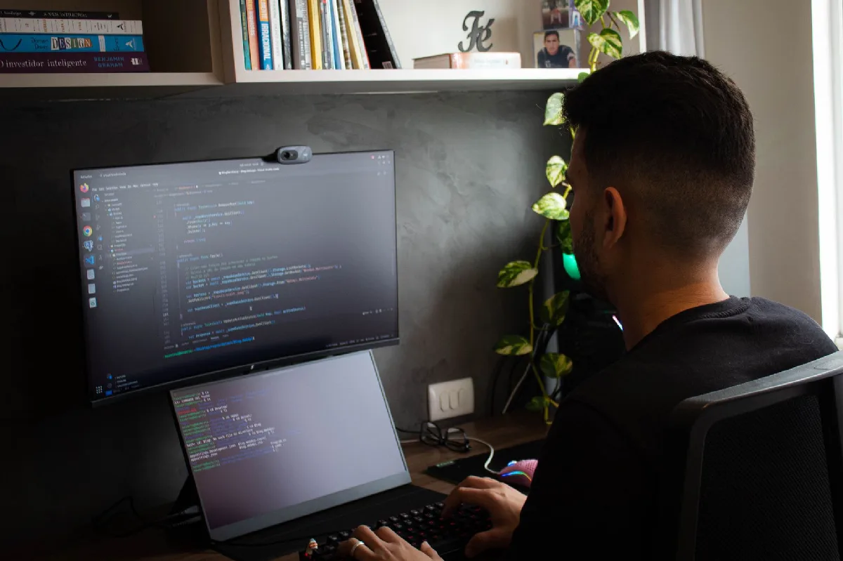 Programador codificando em laptop e monitor em escritório moderno. — Medicina Ocupacional Curitiba