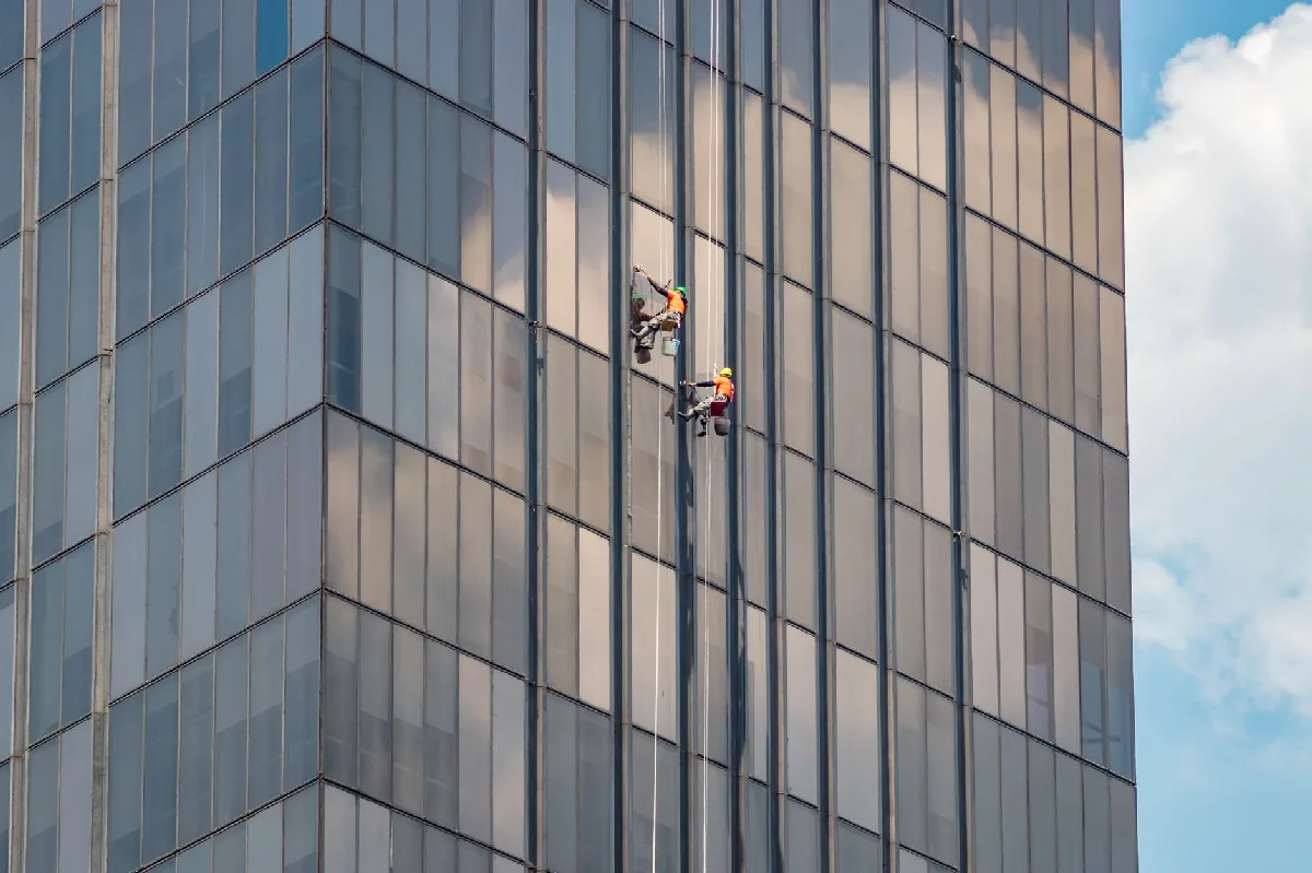 Dois limpadores de janelas trabalham em um prédio de escritórios moderno na Cidade do México. — Medicina Ocupacional Curitiba