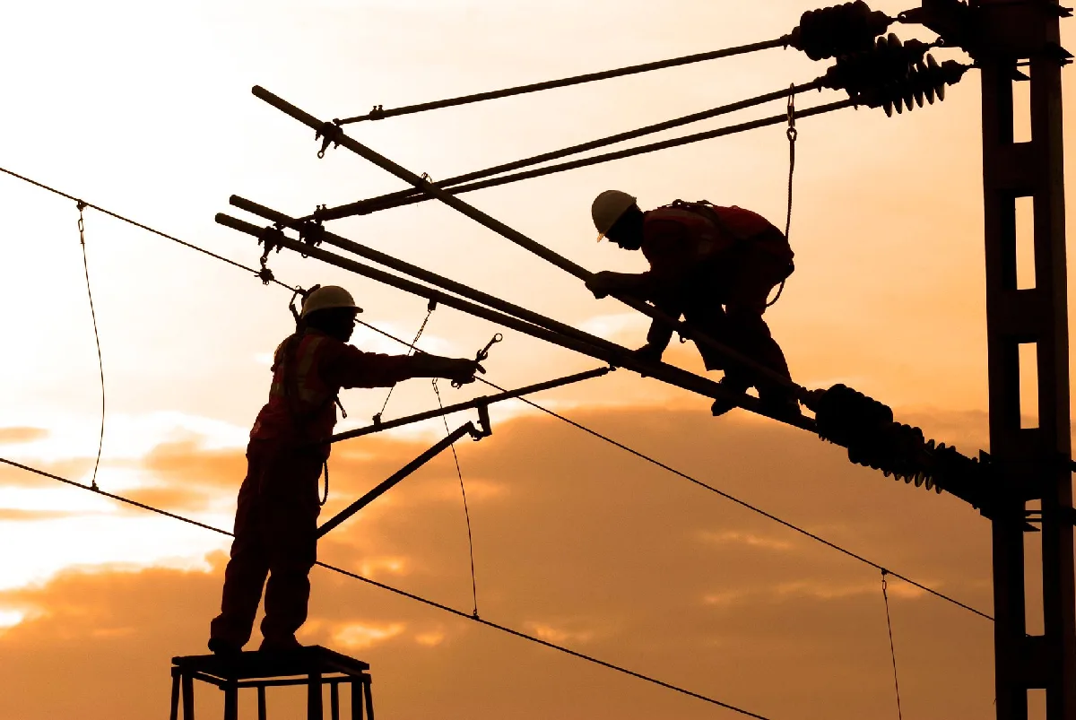 Eletricistas consertam fios de alta tensão ao pôr do sol, demonstrando trabalho em equipe e segurança. — Medicina Ocupacional Curitiba