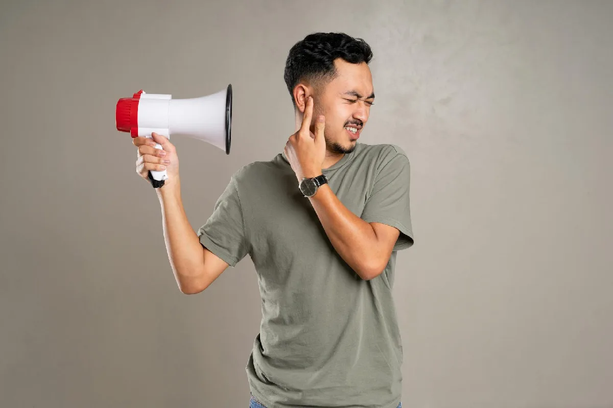 Mapeamento de Ruído: prazos, NRs e responsabilidades em Curitiba Homem com megafone cobre o ouvido em desconforto, representando poluição sonora. — Medicina Ocupacional Curitiba