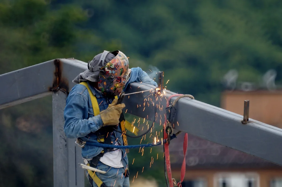 Semana Interna de Prevenção em Curitiba: Fluxo e Riscos Legais Trabalhador da construção civil solda viga de aço ao ar livre, com faíscas e equipamentos de segurança. — Medicina Ocupacional Curitiba